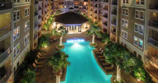 Luxury apartments with resort-style pool, palm trees, spacious sundeck with poolside lounge chairs, grilling station, fountains, and fitness center at Villa Piana Apartments in Dallas