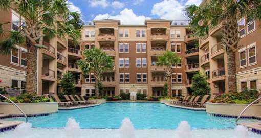 Luxury apartments with resort-style pool, palm trees, spacious sundeck with poolside lounge chairs, grilling station, fountains, and fitness center at Villa Piana Apartments in Dallas