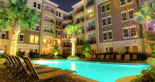 Luxury apartments with resort-style pool, palm trees, spacious sundeck with poolside lounge chairs, grilling station, fountains, and fitness center at Villa Piana Apartments in Dallas