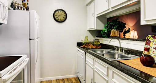 Bright white kitchens with black countertops and wood plank floors at Waters of Winrock Apartments in Houston