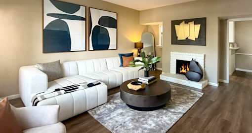 A modern living room with a white sofa, a coffee table, and a fireplace.