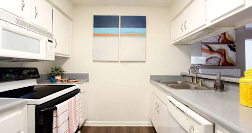bright white kitchen with breakfast bar and wood plank floors at Woodlake on the Bayou Apartments