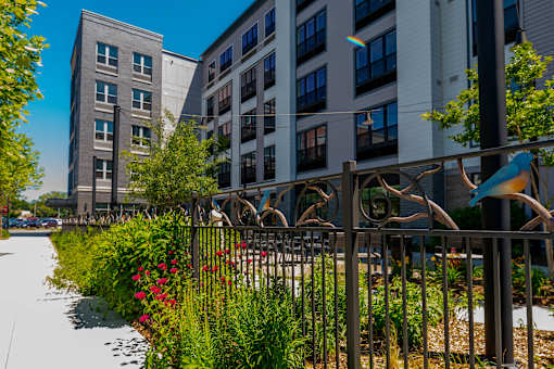 A metal fence with a decorative design separates a sidewalk from a grassy area.