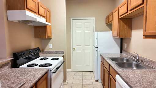 A kitchen with a black stove top oven, a white refrigerator, and wooden cabinets.