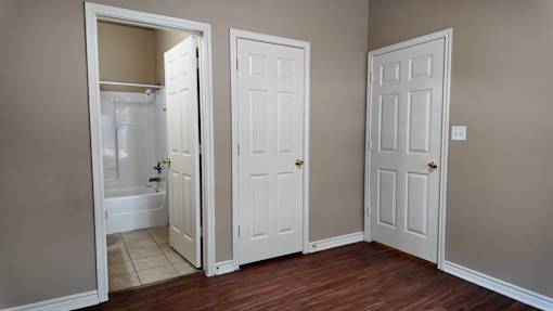 A room with a white door and a white bathroom with a tub and toilet.