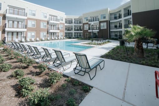 a swimming pool with chaise lounge chairs and a palm tree in front of an apartment building