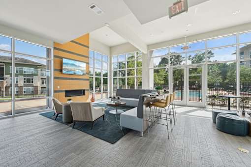 A modern community room with a fireplace and floor to ceiling windows, offering a view of the outdoors.