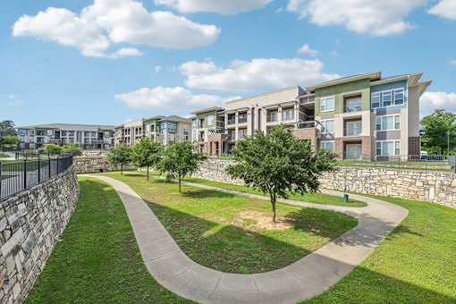 A stone wall borders a grassy area with a concrete walkway and a tree.