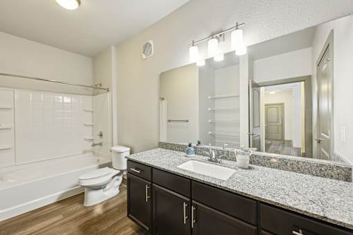 A brightly lit bathroom with a white toilet, a sink, and a large mirror.