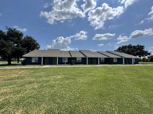 A large building with a grey roof is surrounded by a grassy field.