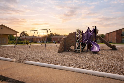A playground with a purple slide and a brown building in the background.