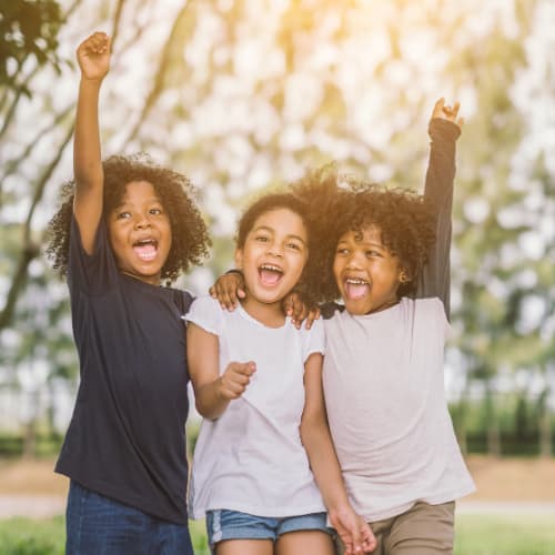 Three children are playing outside with their arms in the air.