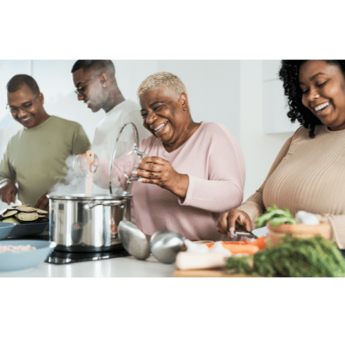 A group of people are gathered around a kitchen counter, cooking and laughing together.