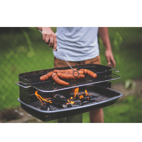 A person grilling sausages and vegetables on a barbecue.