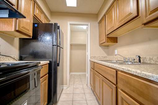 A kitchen with a black refrigerator and wooden cabinets.