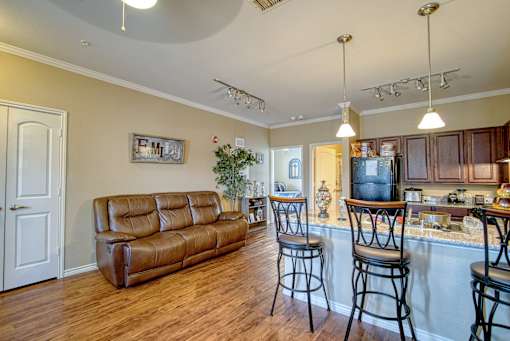 A kitchen with a bar and stools is adjacent to a living room with a couch and a plant.
