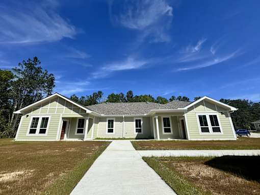 A house with a grey roof and white walls is surrounded by a grassy area.