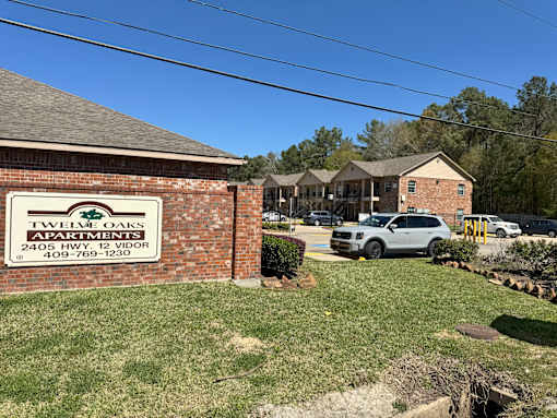 A sign for Twelve Oaks Apartments is in front of a brick building.