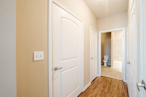 A hallway with a white door and a toilet visible in the distance.