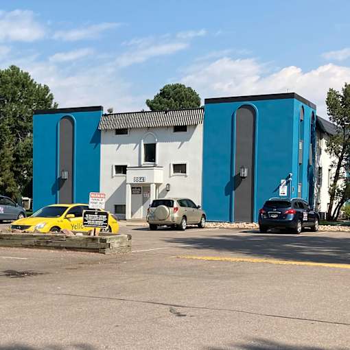 A yellow car is parked in front of a white and blue building.
