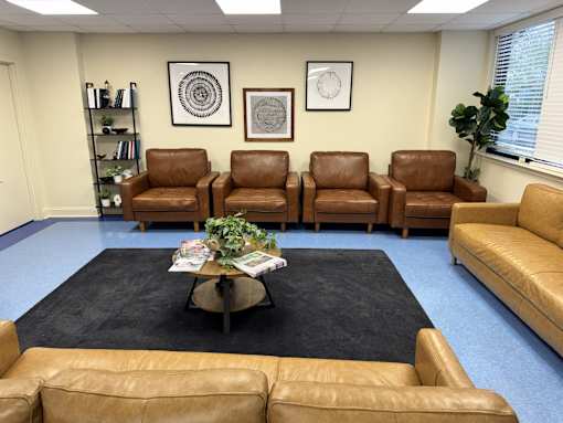 A waiting room with brown leather chairs and a coffee table with magazines and a plant.