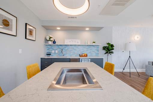 A modern kitchen with a marble table and yellow chairs.