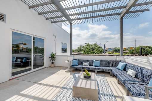 A patio with a white pergola and blue cushioned seating.