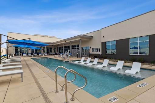 Resort-style swimming pool with lounge chairs and apartment building in the background