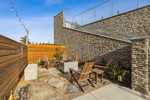A patio with a stone wall and wooden chairs.