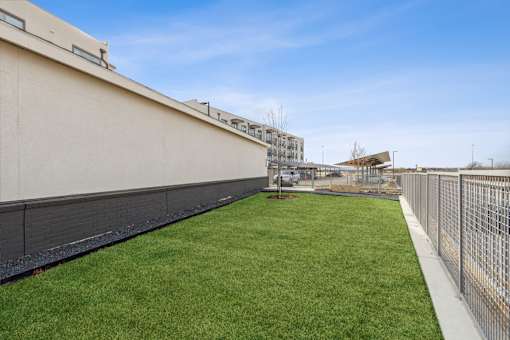 A grassy area in front of a building with a fence on the right side.