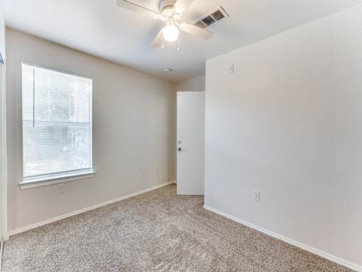 A room with a carpet floor, a ceiling fan, and a window with blinds.