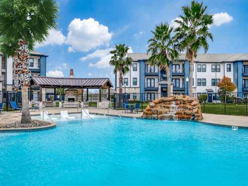 A swimming pool surrounded by palm trees and a building in the background.