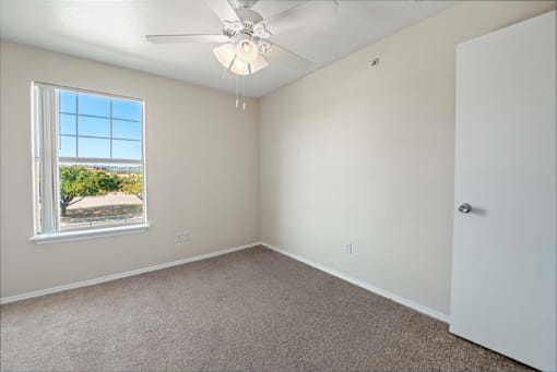 A room with a ceiling fan and a window overlooking a tree-filled landscape.