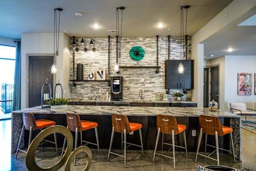 A modern kitchen with a bar area featuring a stone backdrop and bar stools at The Grand at Manor Apartments, Texas
