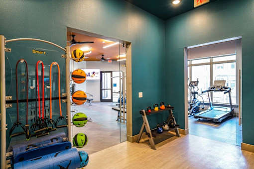 A gym with a row of exercise equipment including a treadmill, a rowing machine, and a stationary bike at The Grand at Manor Apartments, Texas