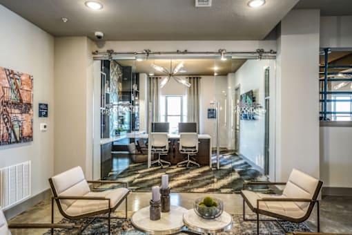A space wit white chairs, a coffee table and a small glass office with two monitors and chairs in the foreground, Manor