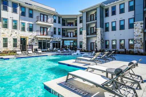 A swimming pool with sun loungers in front of apartment buildings at The Grand at Manor Apartments, Manor, TX, 78653