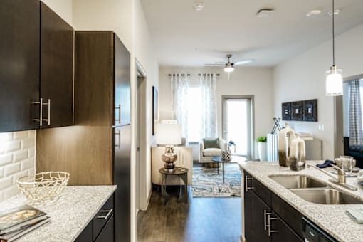 Wooden cabinets with granite countertops and a a couch in a living room in the foreground,