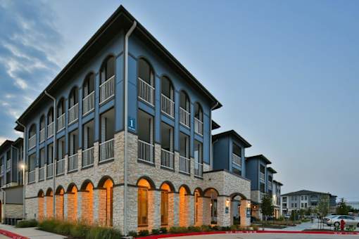 A modern building with a stone facade and arched windows at The Grand at Manor Apartments, Texas