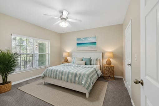 A bedroom with a bed, a ceiling fan, and a painting of a beach scene on the wall.