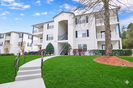 A white apartment building with a tree in front.