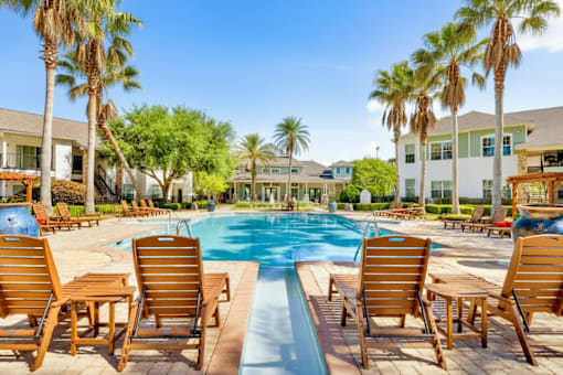 A pool surrounded by wooden chairs and palm trees.