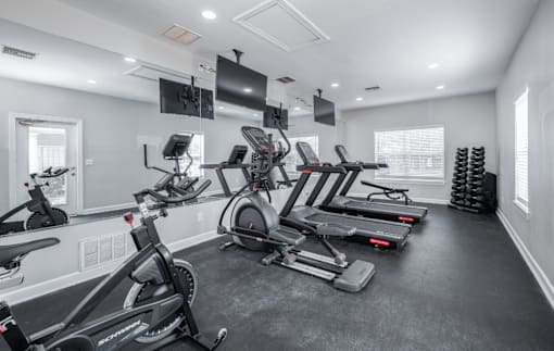 A gym with treadmills, exercise bikes, and a television.