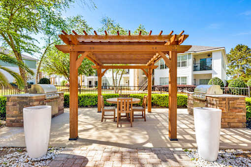 A wooden pergola with a bench and two pillars in front of a building.