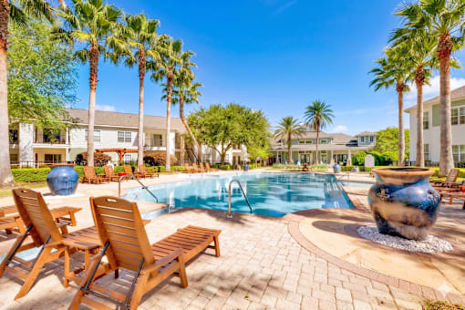 A pool surrounded by palm trees and wooden chairs.