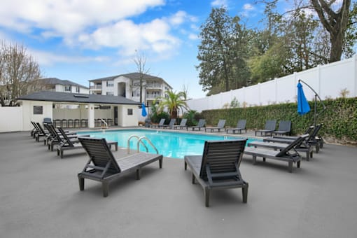 A pool surrounded by lounge chairs and a white fence.