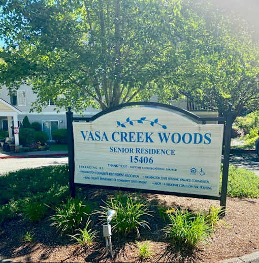 A sign for Vasa Creek Woods Senior Residence is displayed in front of a tree.