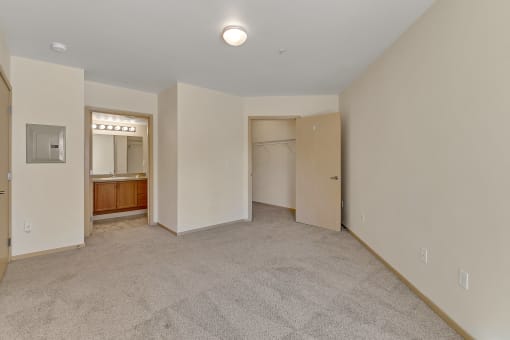 a spacious living room with white walls and carpet and a door to a bathroom