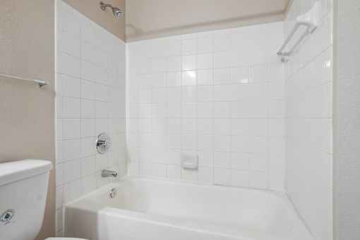 A white bathtub in a bathroom with a shower head and a toilet.
