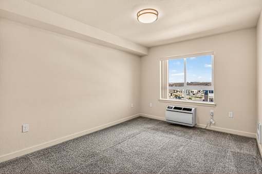 A room with a window showing a view of a parking lot and a wall-mounted air conditioner.